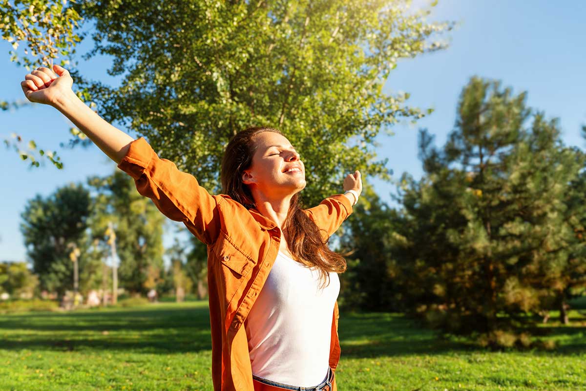 Woman enjoying morning sunlight in a grassy field.